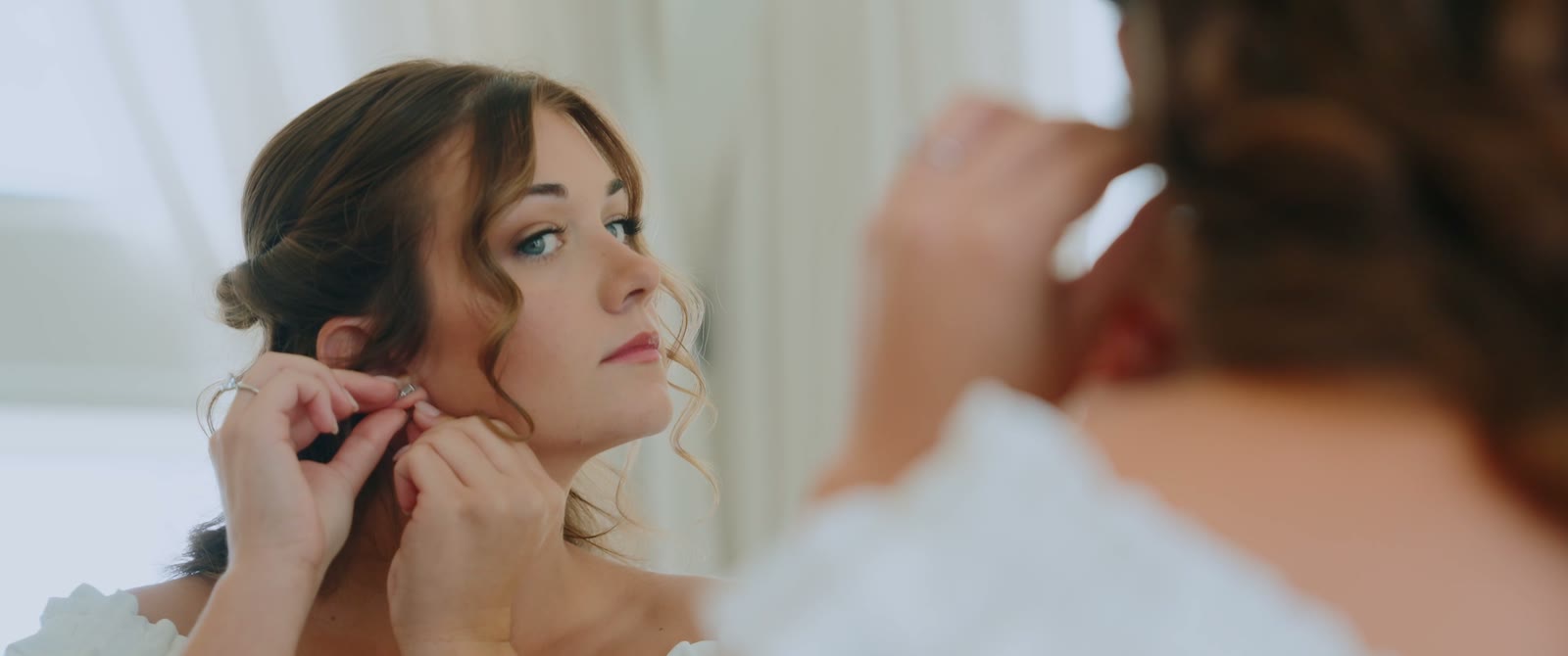 The bride puts on her earrings in the mirror while getting ready, a still from Jacey and Ryan's film.