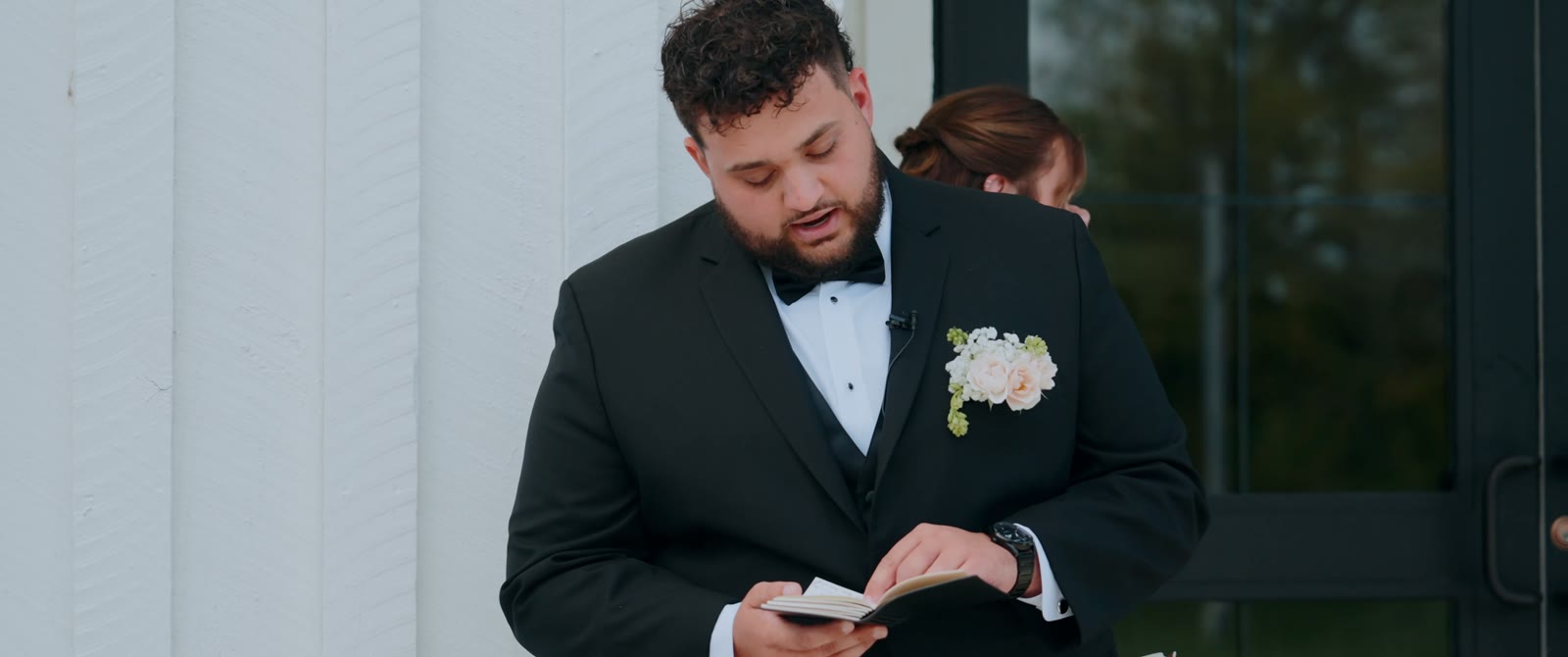 The groom reads his vows from a small book outside a white building at The Sixpence.