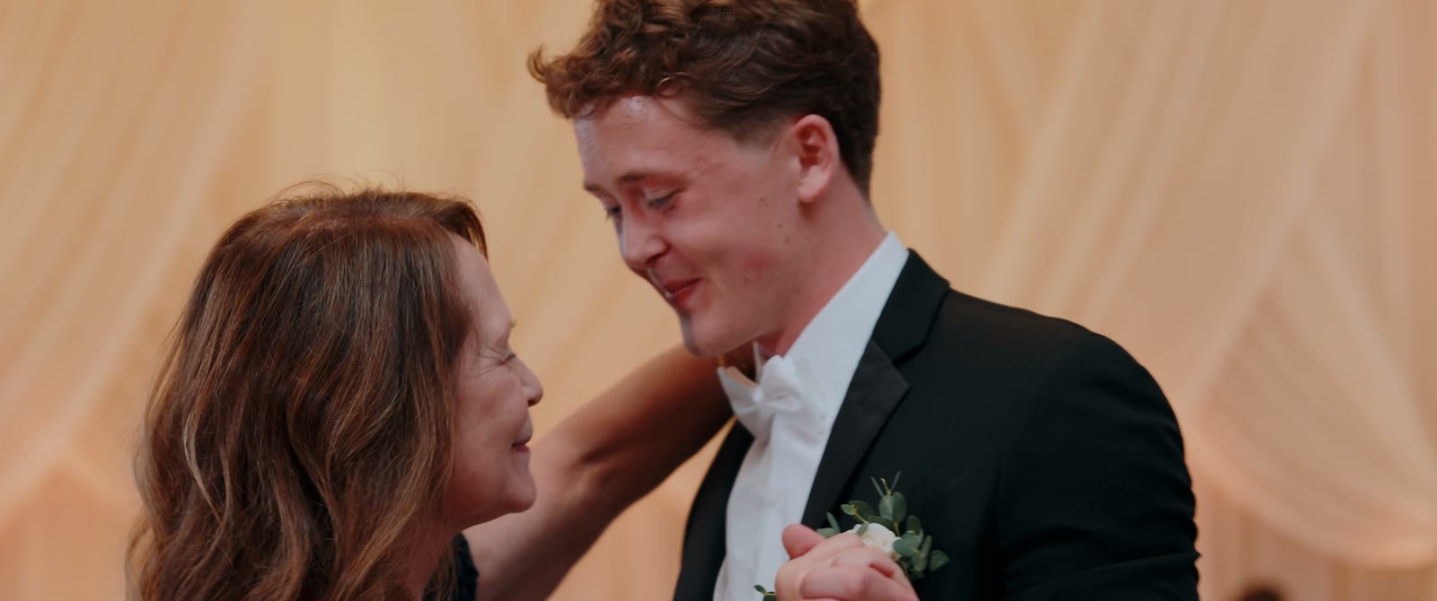 The groom smiles as he shares a dance with an older woman at the reception.