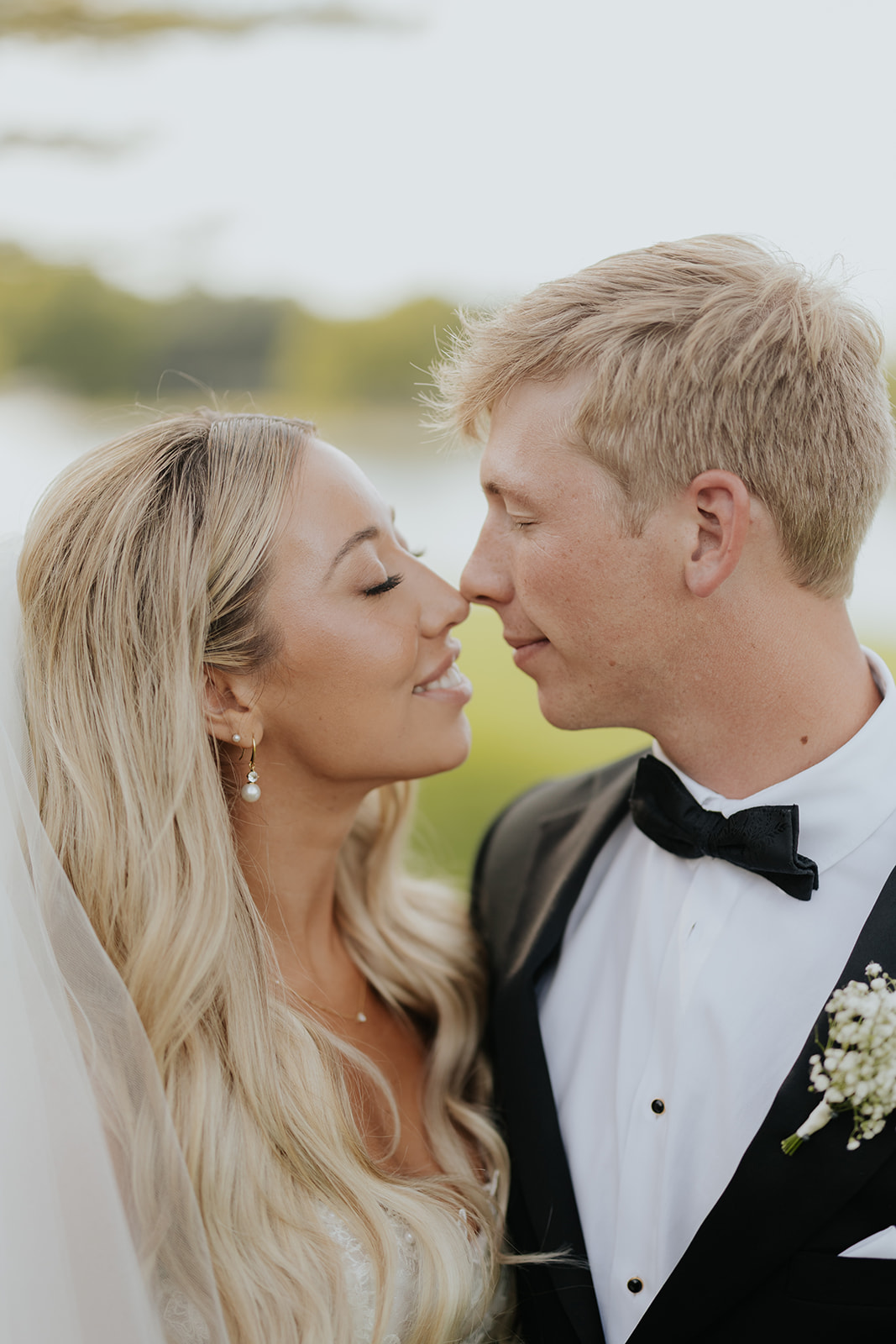 Lauren and Grant lean in nose to nose, smiling with eyes closed in an outdoor portrait.