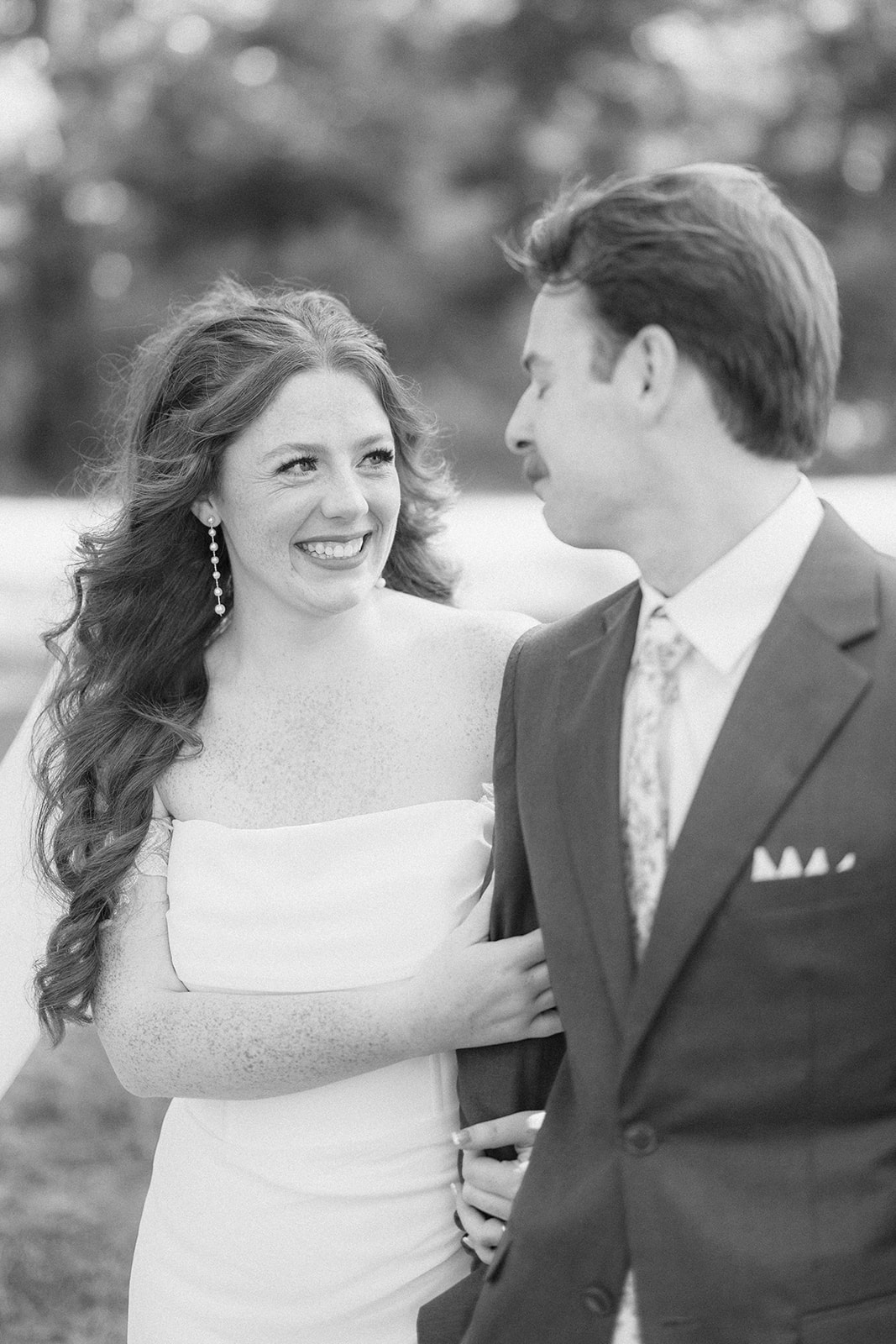 Black and white of Maci and Matt arm in arm, the bride beaming as she looks up at him.