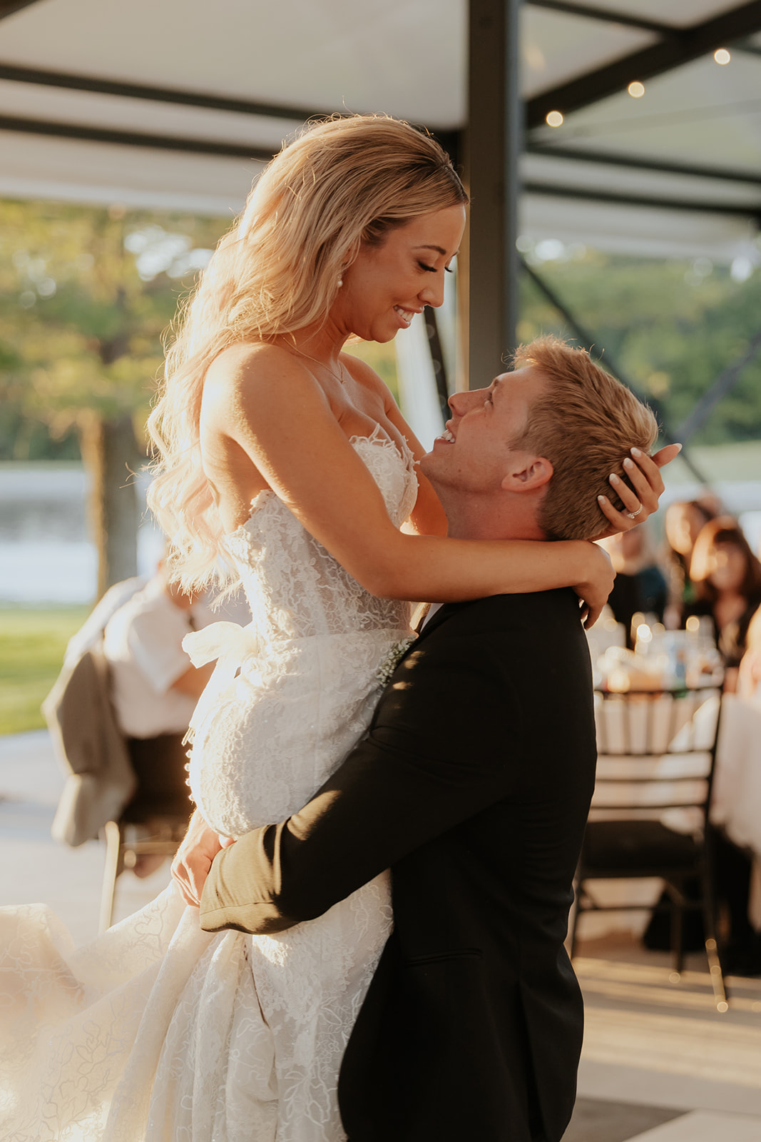 The groom lifts the bride during their first dance as guests watch from reception tables.