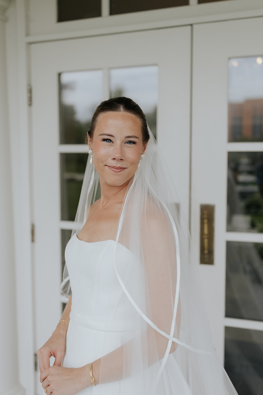 Brooklyn smiles softly in her strapless gown and veil in front of white French doors at Ritz Charles