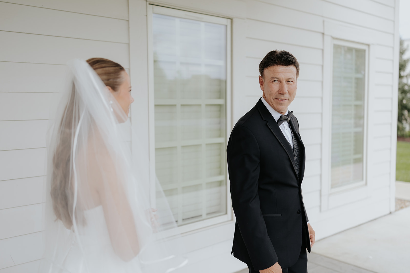 The bride walks up behind a man in a tuxedo for a first look as he glances back over his shoulder