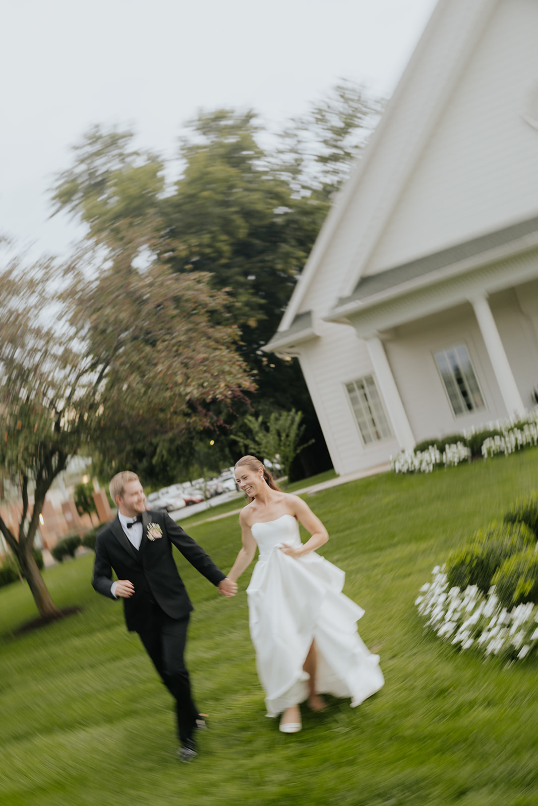 Brooklyn and Jared run hand in hand across the lawn outside the white chapel at Ritz Charles