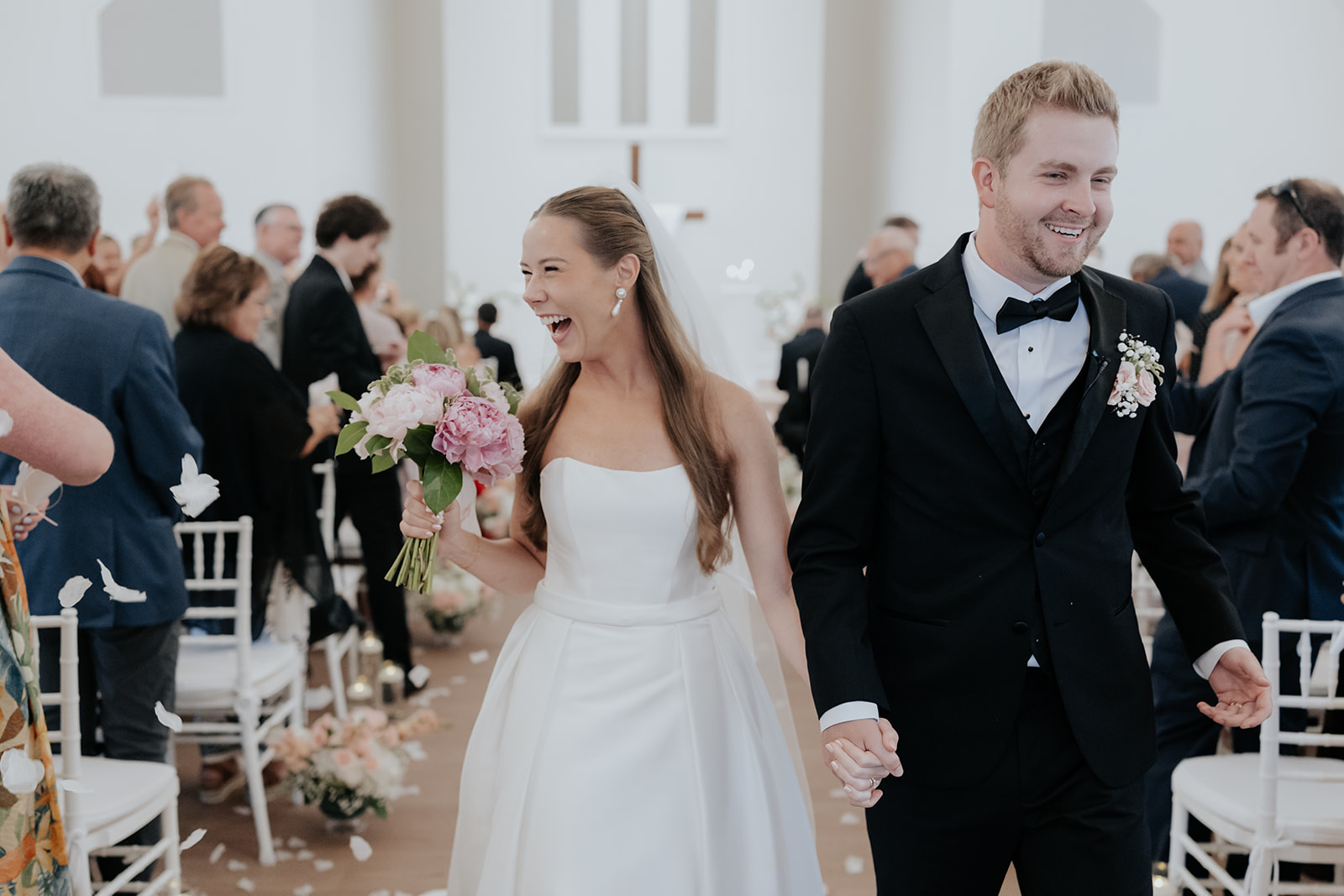 Brooklyn laughs with her pink peony bouquet as she and Jared walk back up the aisle under falling petals