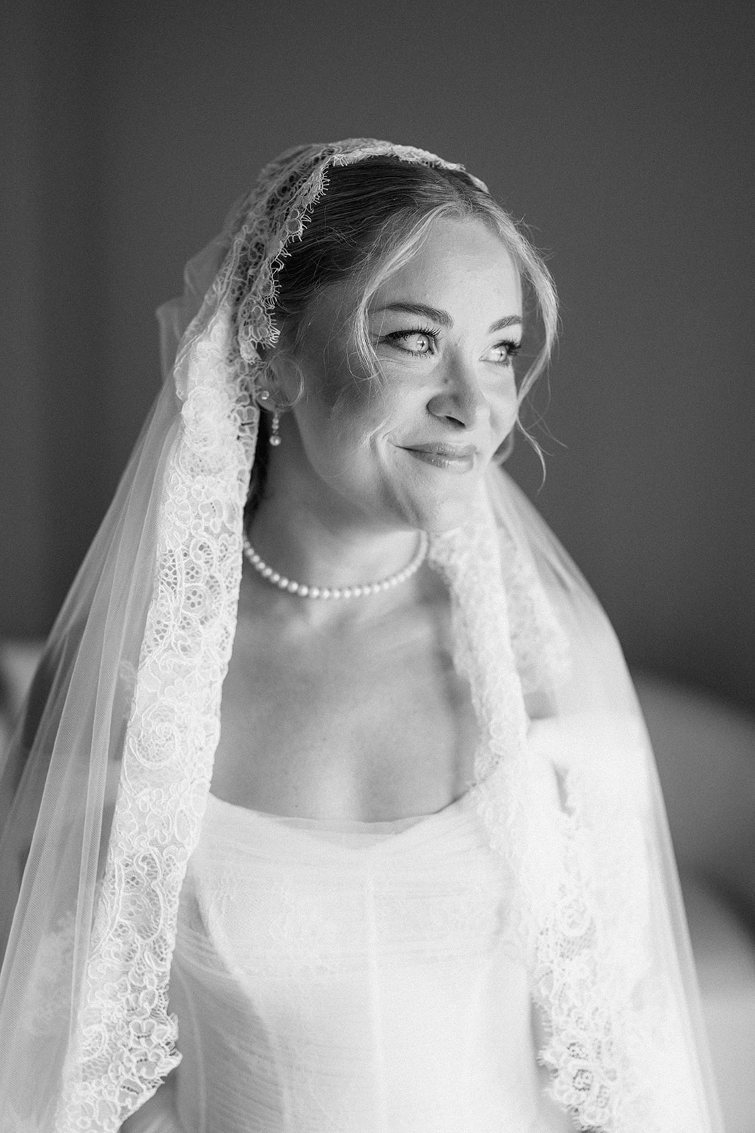 Black and white portrait of the bride smiling softly beneath her lace-edged veil and pearls.
