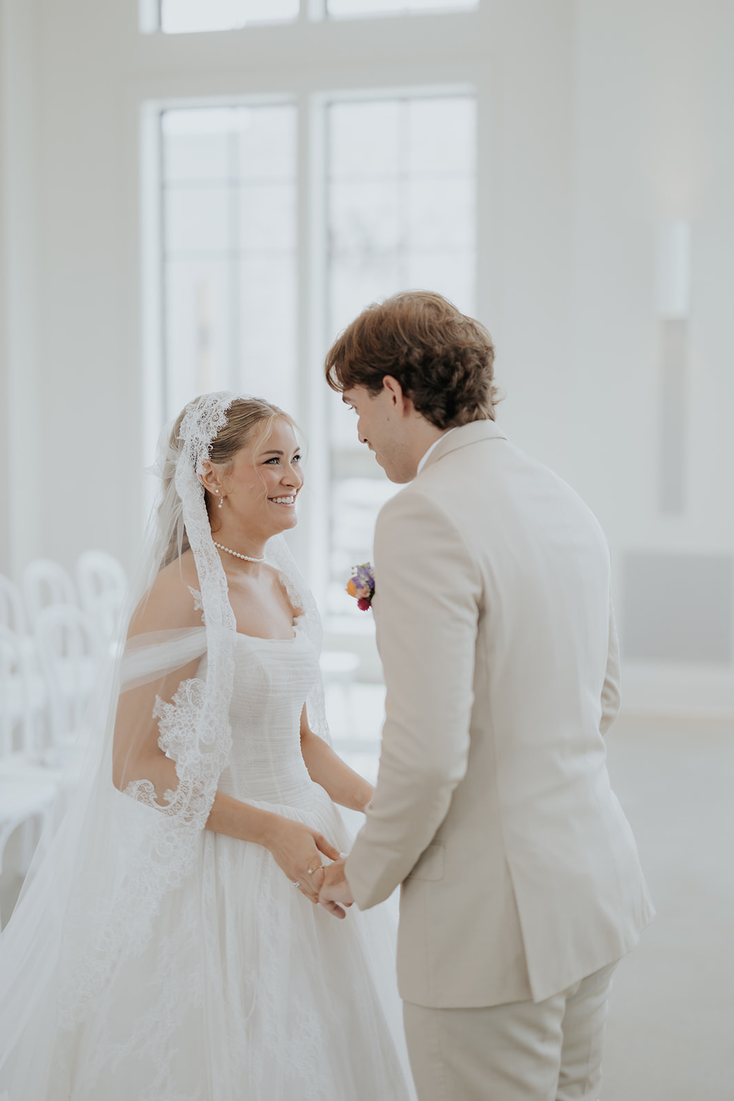 The bride smiles up at the groom in his cream suit as they hold hands after their first look.