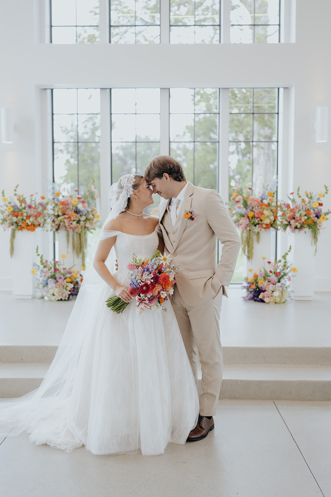 Cami and Trey touch foreheads at the altar, framed by bright, colorful floral arrangements.