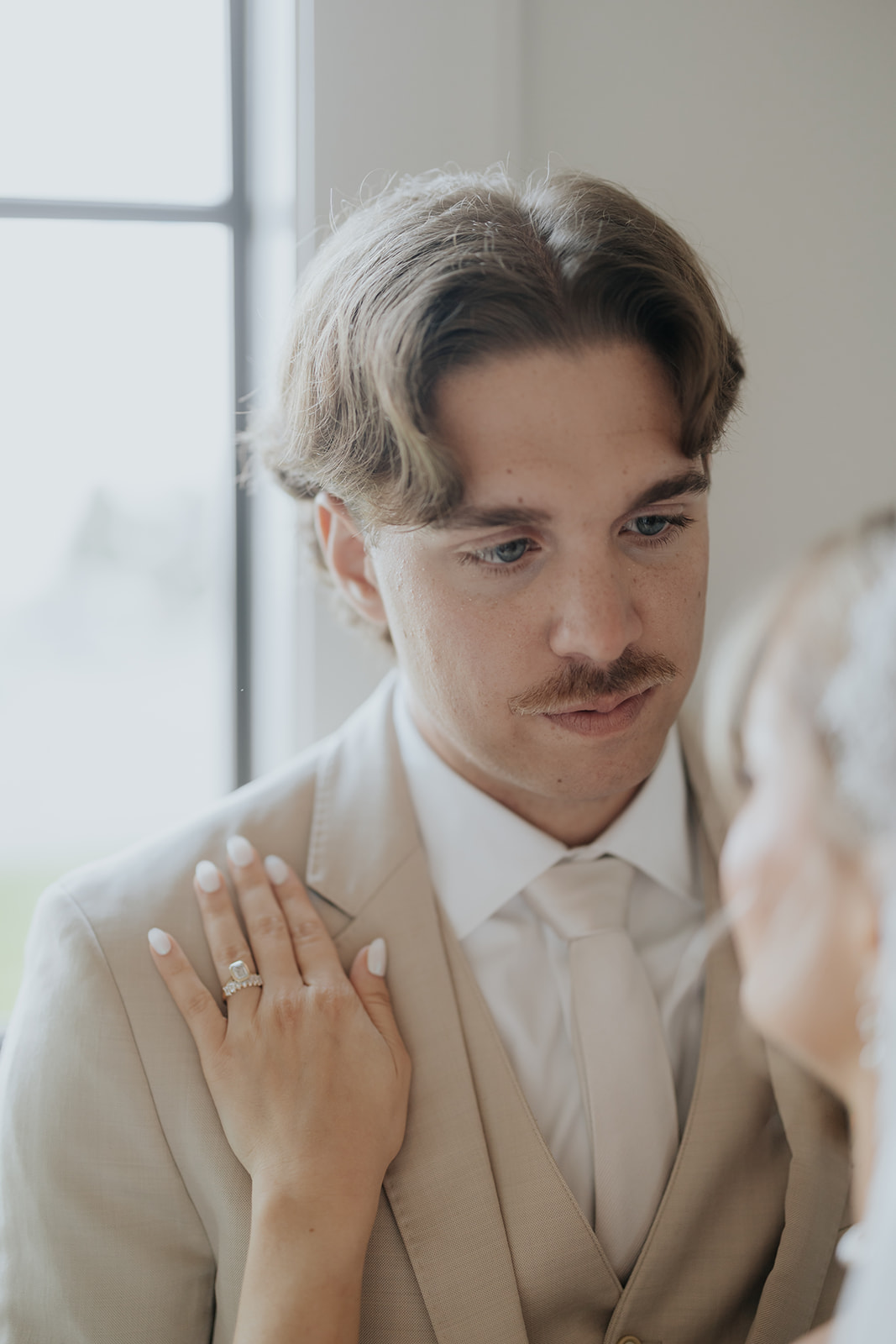 The groom gazes at the bride as her hand, wearing her engagement ring, rests on his lapel.