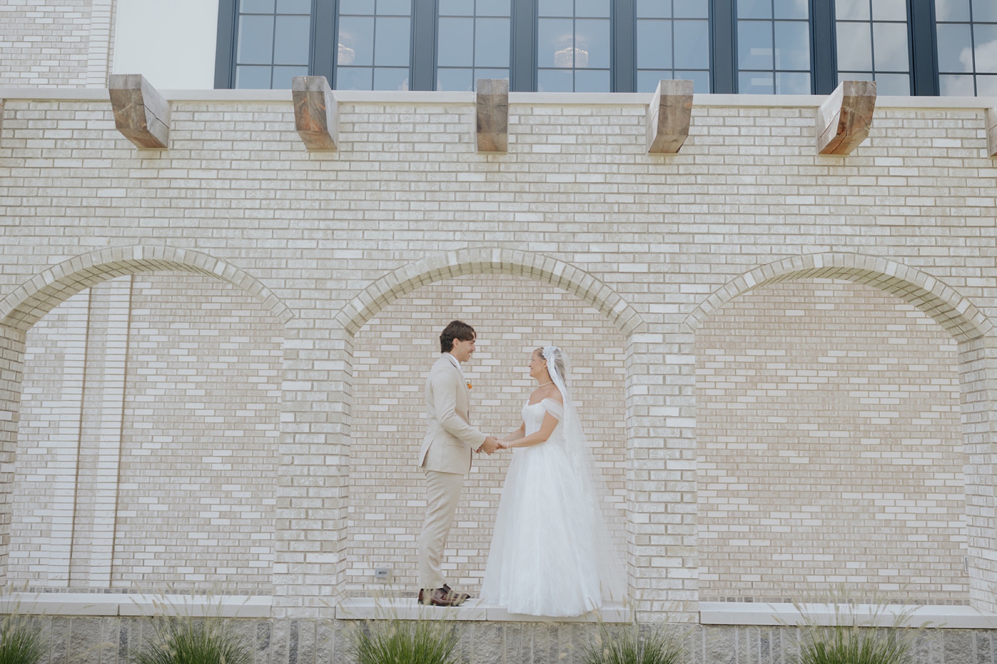 Cami and Trey hold hands beneath the brick arches outside Westwood Vowery & Estate.