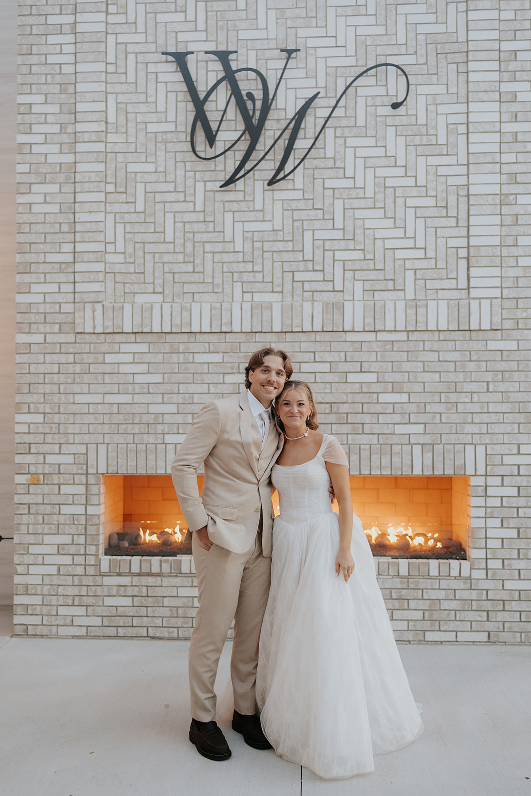 Cami and Trey stand by the outdoor fireplace beneath the Westwood Vowery & Estate monogram.