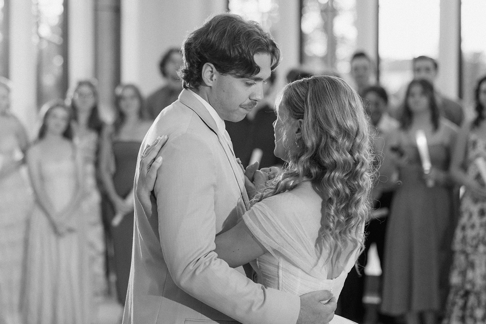Black and white photo of Cami and Trey sharing their first dance as guests look on.