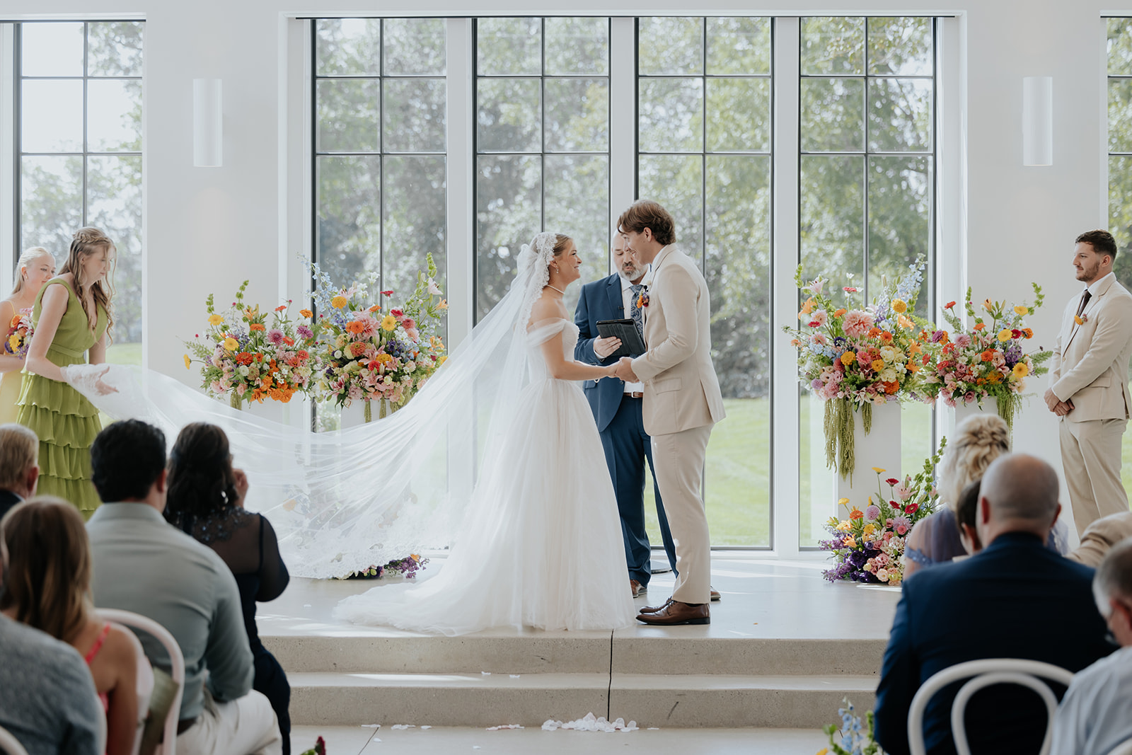 Cami and Trey hold hands at the altar as the bride's cathedral veil sweeps across the steps.