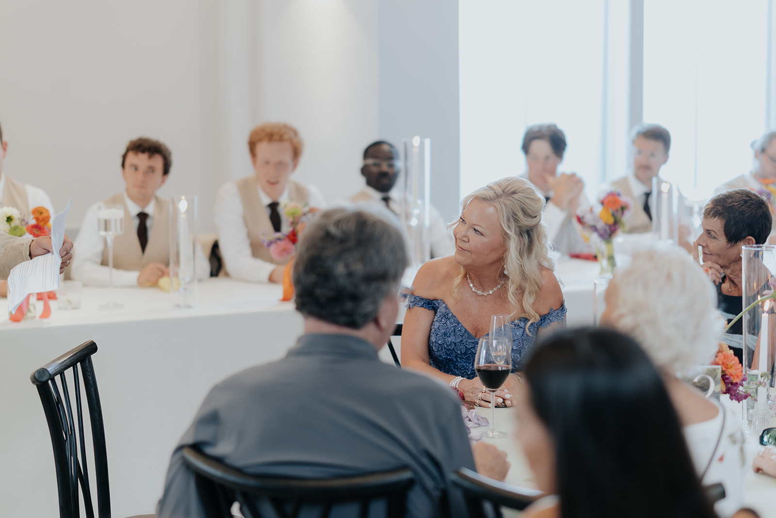 Guests and groomsmen listen and smile at the reception tables during the toasts.