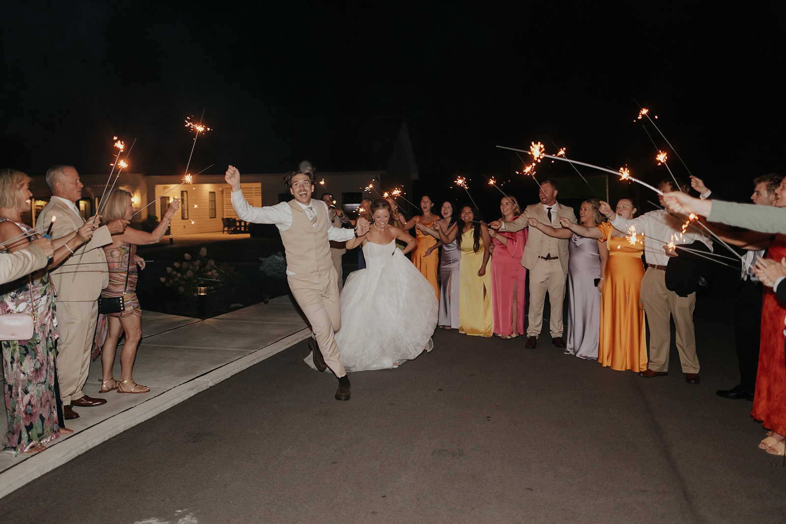 Cami and Trey run hand in hand through a tunnel of sparklers held by family and friends.