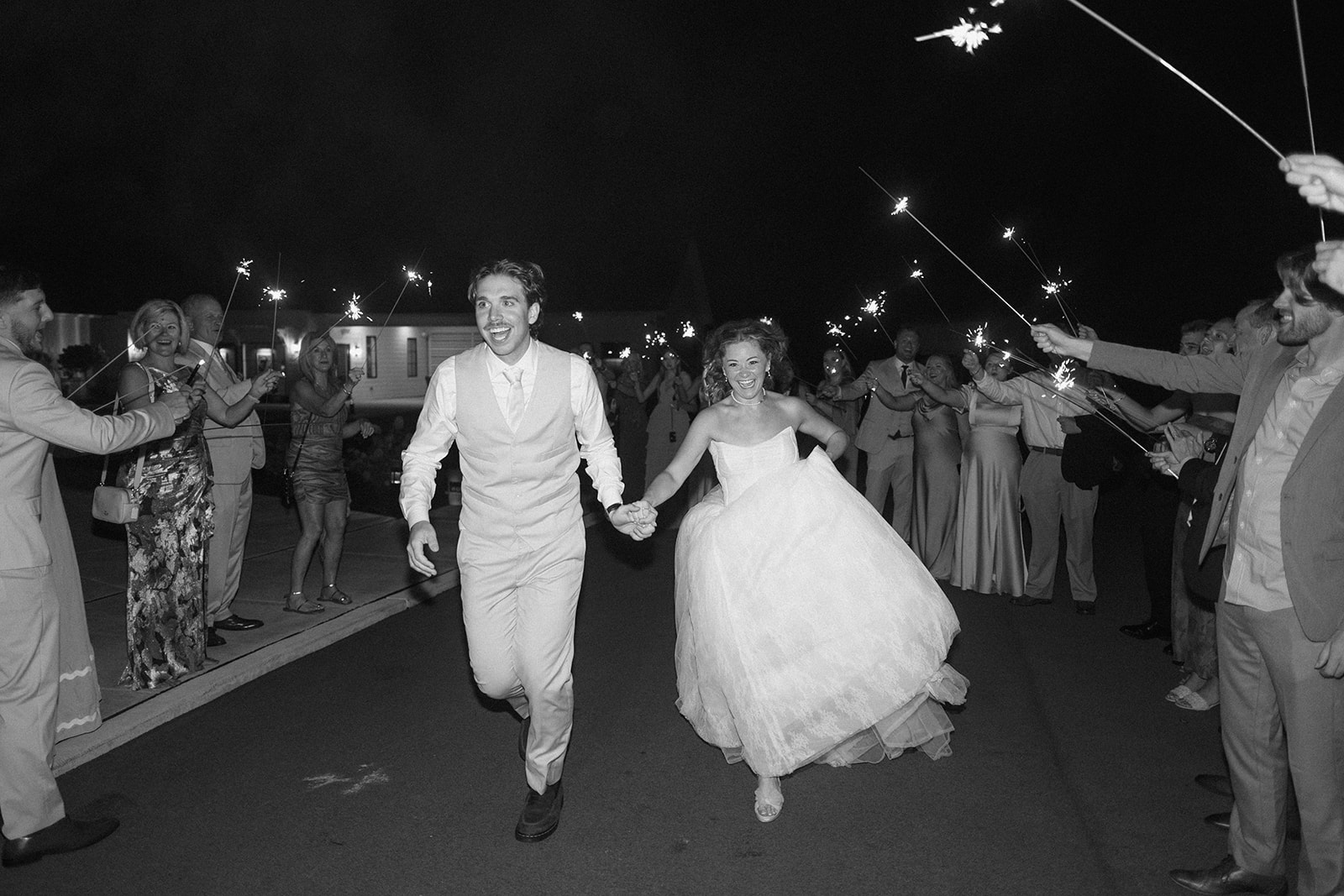 Black and white photo of Cami and Trey running hand in hand through their sparkler exit.