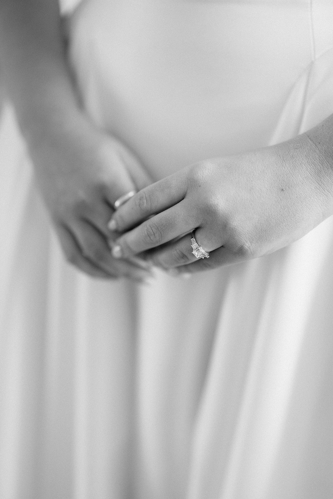 Black and white close-up of the bride's hands showing her engagement ring against her gown