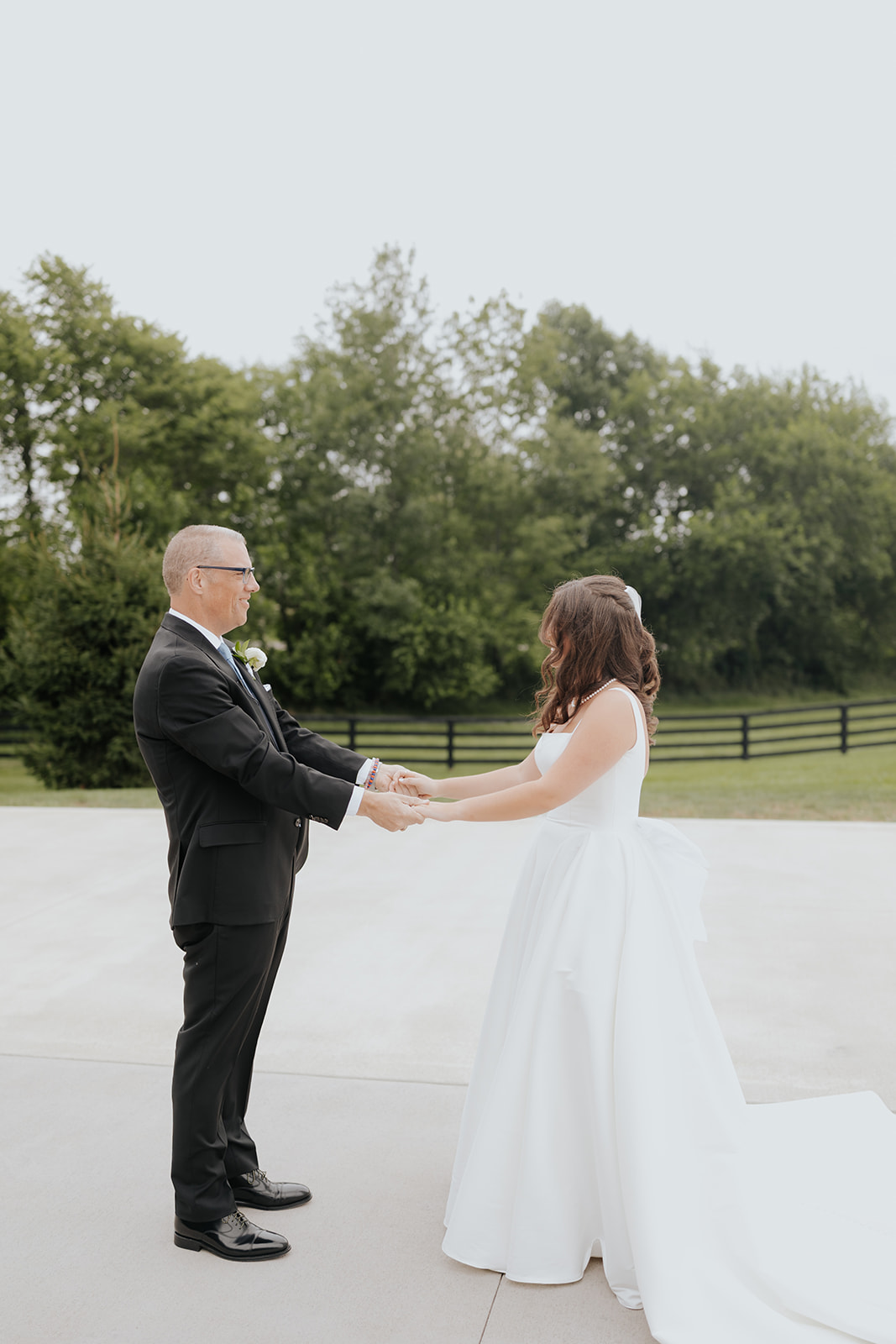 The bride holds hands with an older man in a suit during a first look on the patio