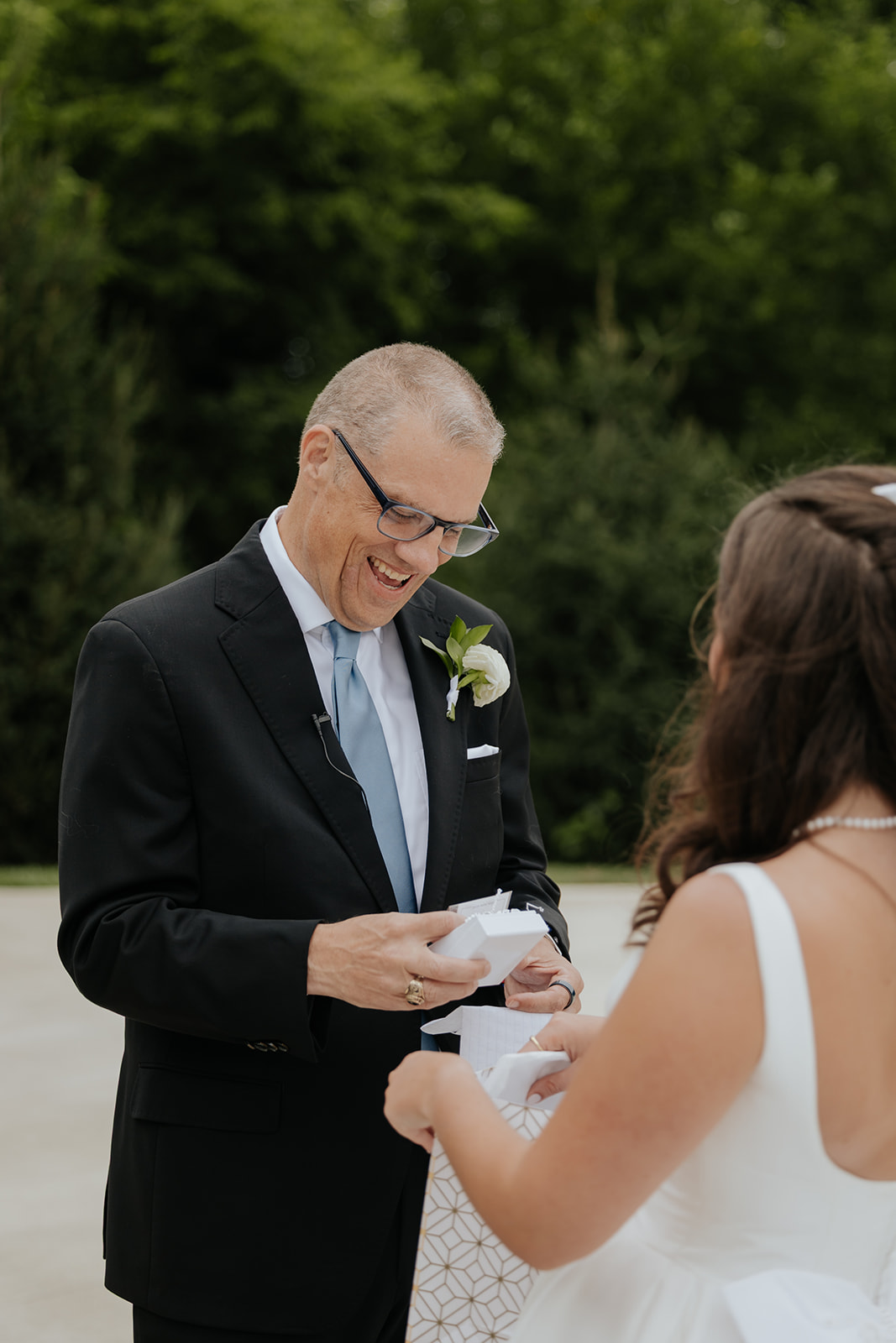A man in glasses laughs as he opens a small gift from the bride before the ceremony