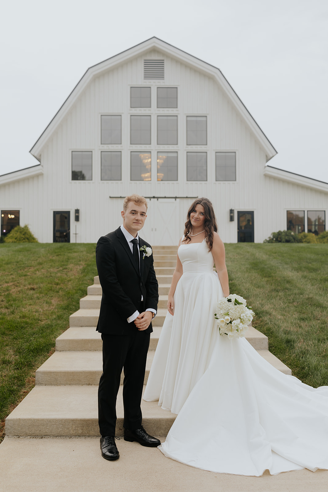 Cody and Kristen pose on the steps in front of the white barn at The Sixpence