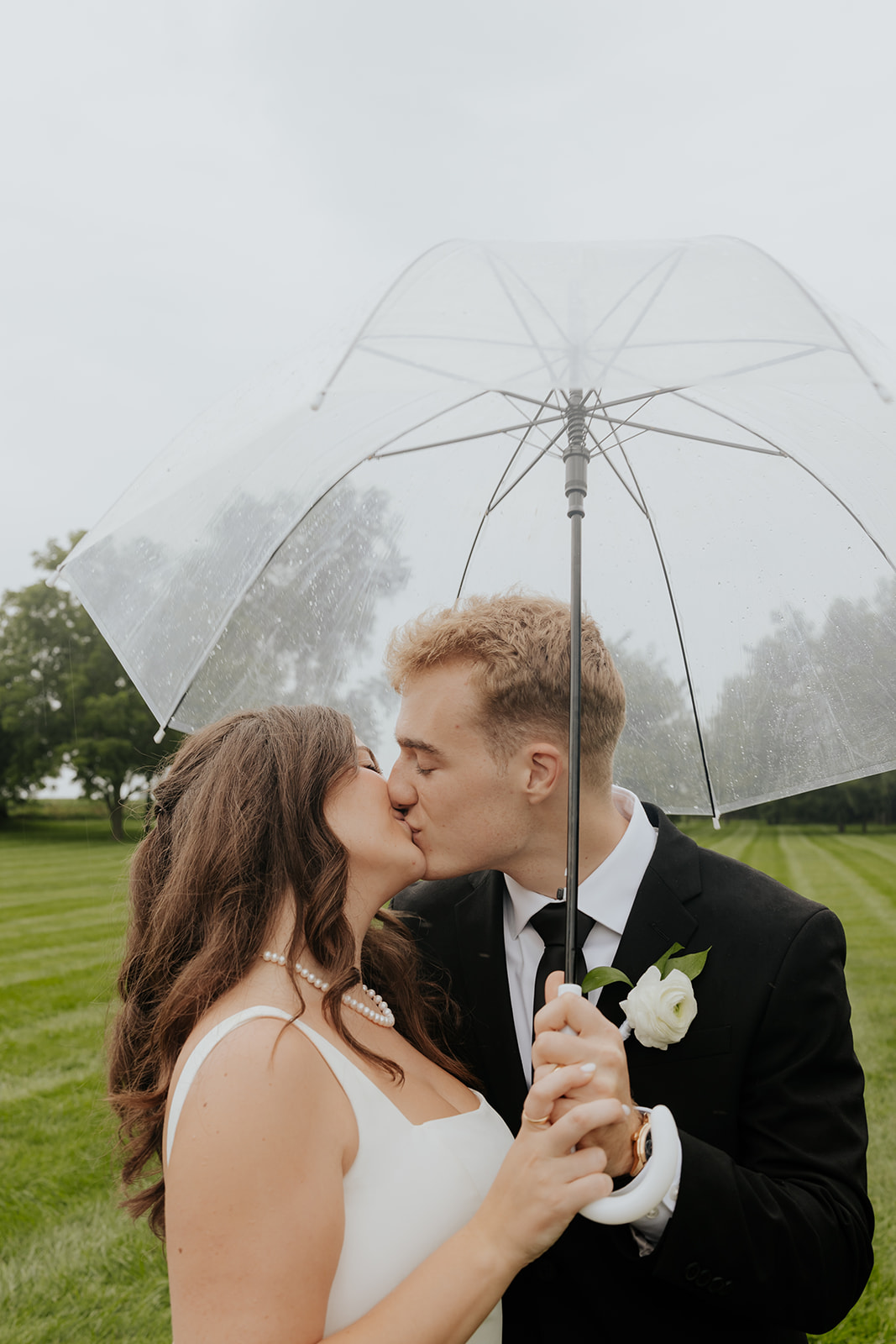 Cody and Kristen kiss under a clear umbrella on a misty, overcast wedding day