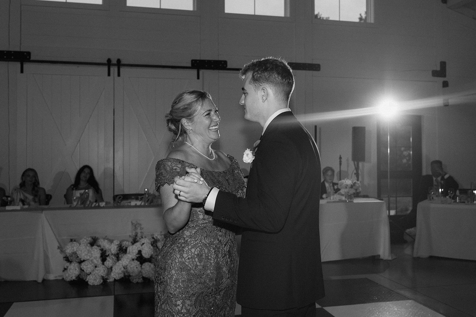 Black and white photo of the groom sharing a dance with a smiling woman at the reception
