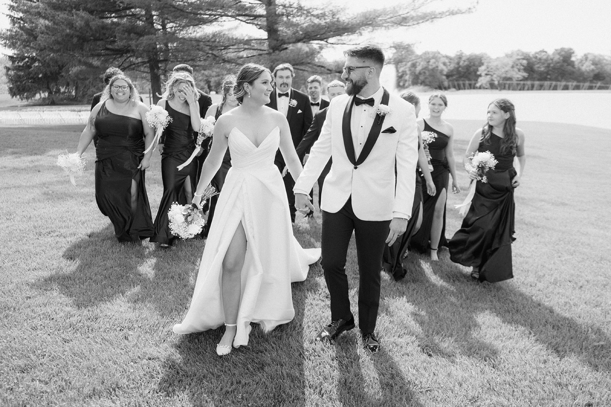 Black and white photo of Dallas and Beau laughing as they walk across the lawn with their wedding party