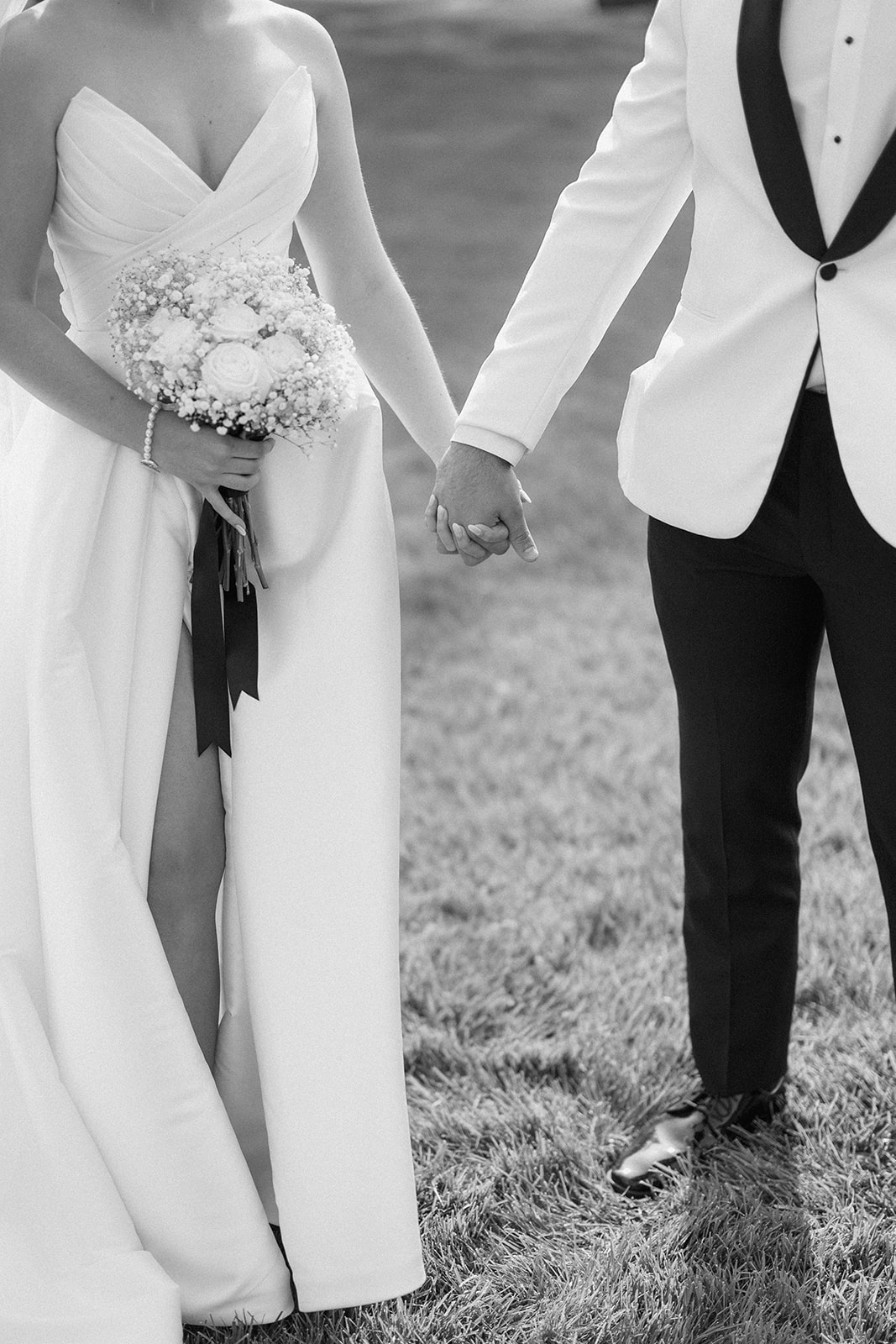 Black and white close-up of Dallas and Beau holding hands, her bouquet tied with black ribbon