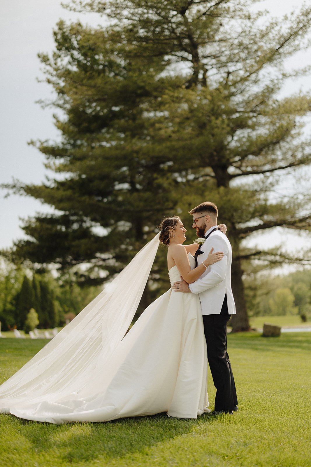 Dallas and Beau embrace beneath a tall pine as her cathedral veil trails across the grass