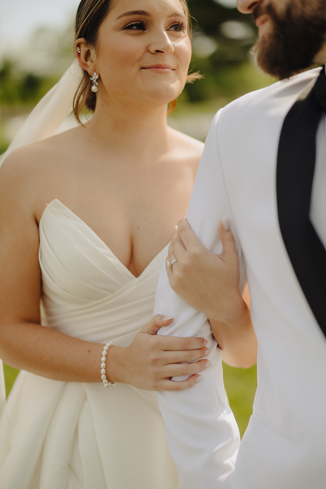 The bride smiles softly while holding the groom's arm in his white dinner jacket