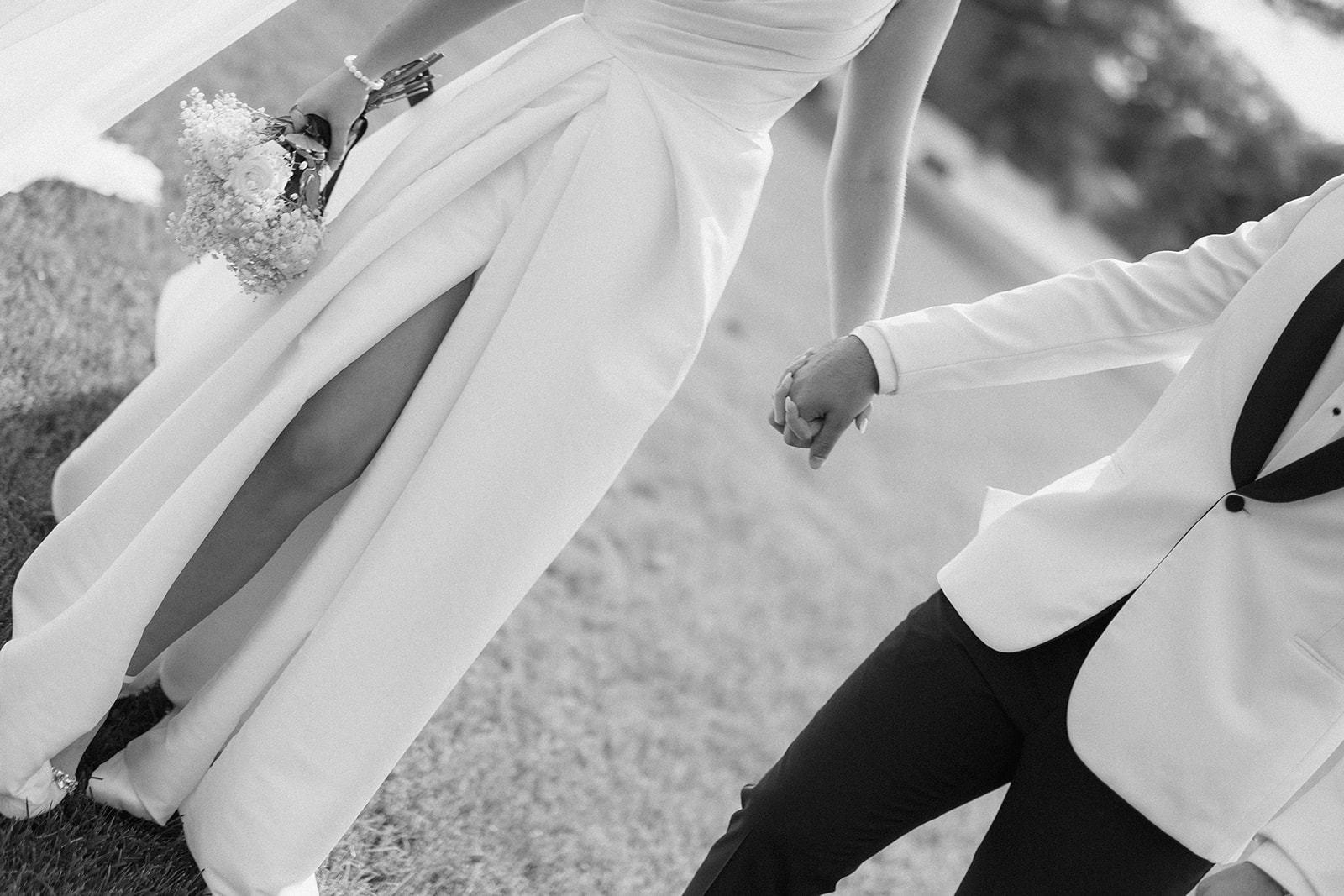 Black and white detail of Dallas and Beau's joined hands as they stride across the grass