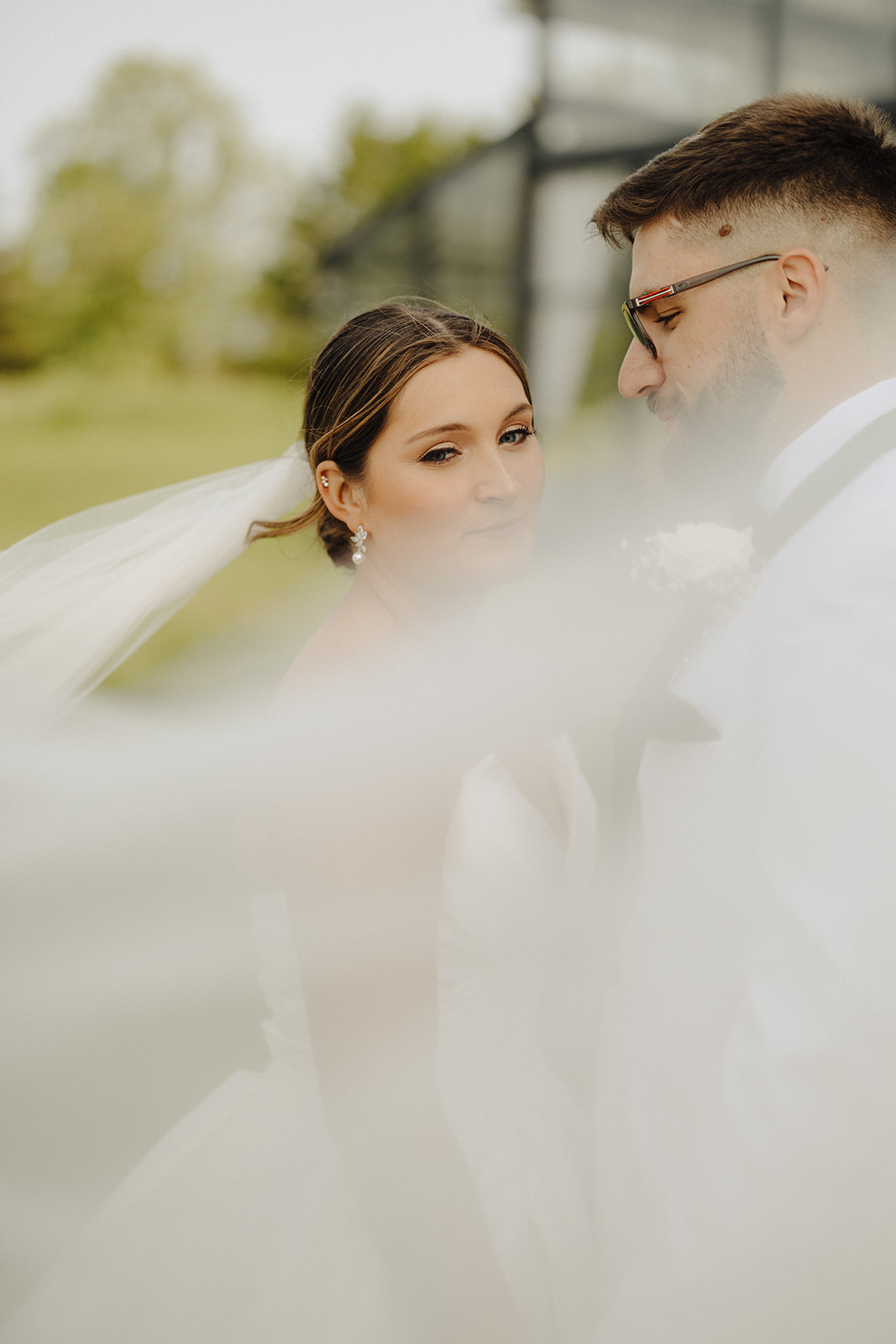 Dallas and Beau stand close as the bride's veil drifts across the frame in a soft outdoor portrait.