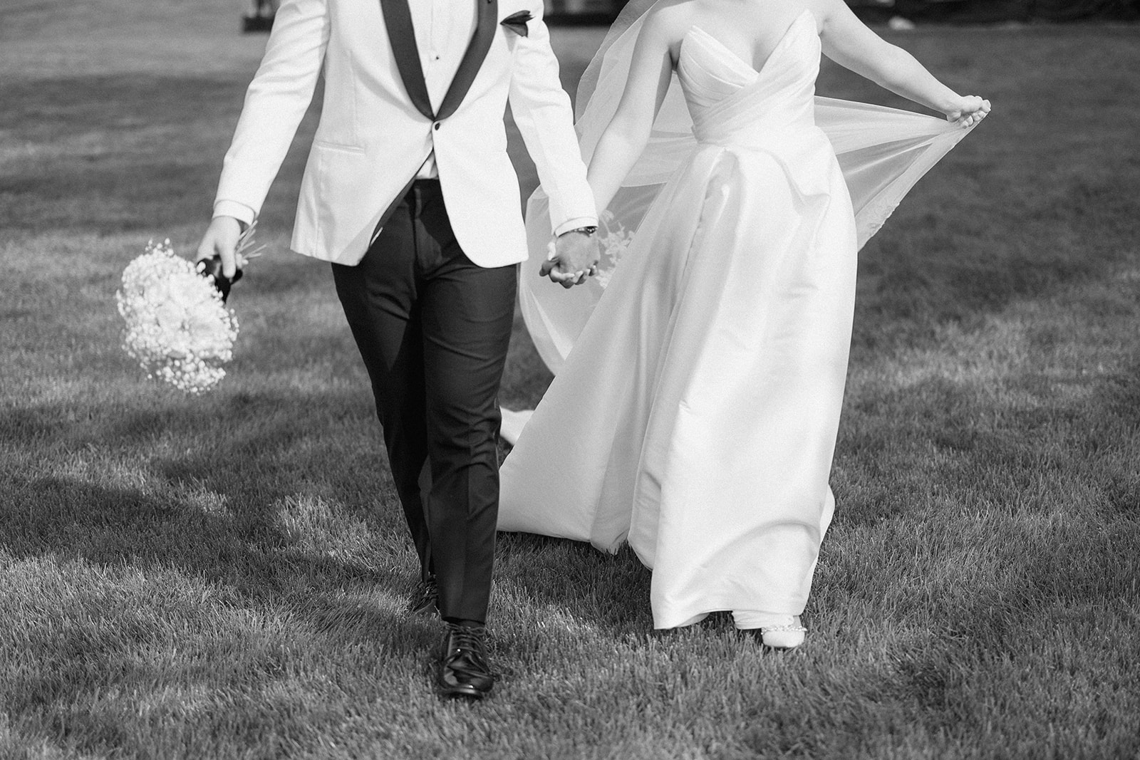 Black and white of Dallas and Beau walking hand in hand across the lawn, bouquet in his hand.