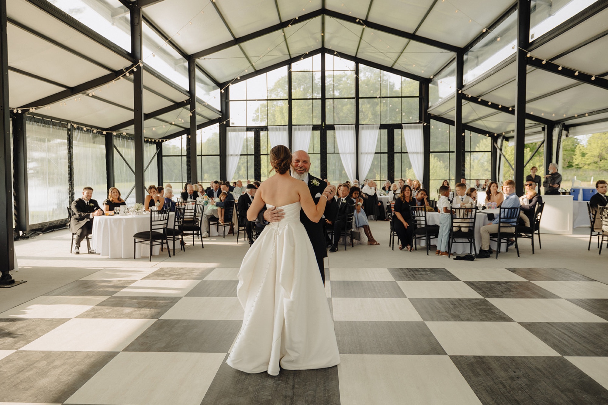 The bride dances with her father on the checkered dance floor inside the glass pavilion at The Clubhouse.
