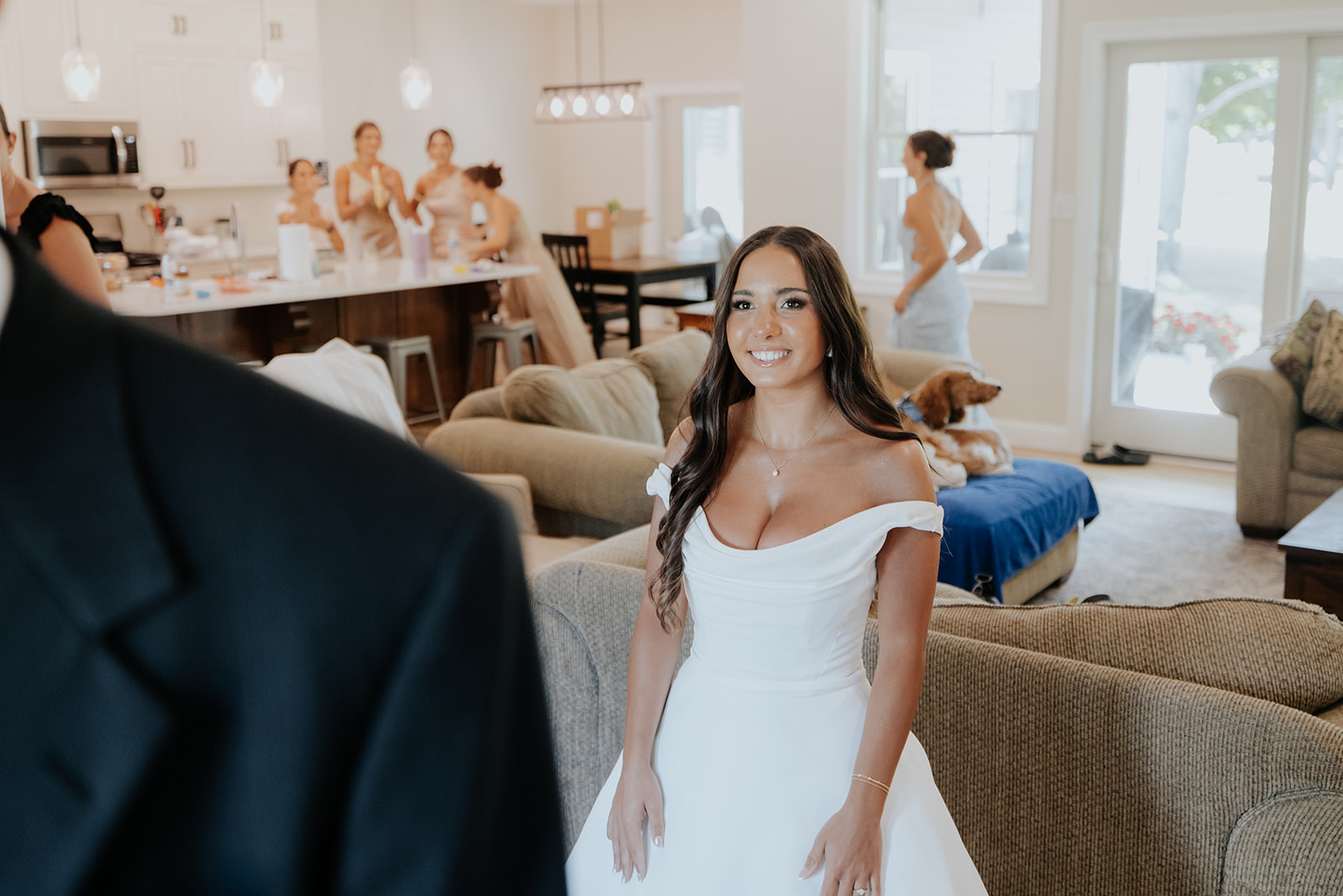 The bride smiles at the groom during their first look as her bridesmaids watch from the kitchen.