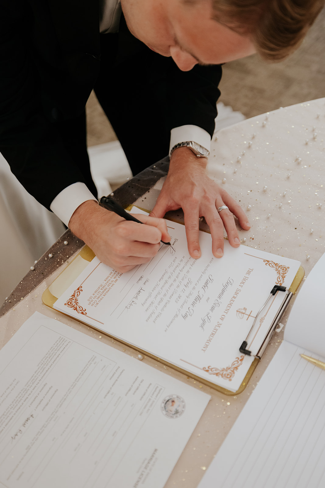 The groom signs the marriage certificate on a gold clipboard after the ceremony.