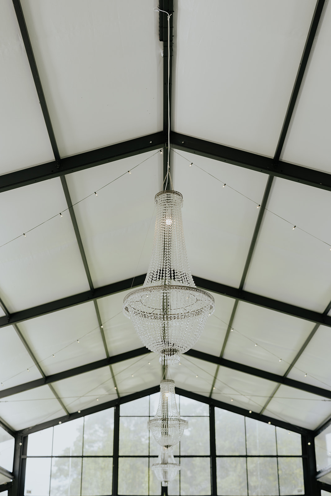 Crystal chandeliers hang from the peaked glass and steel ceiling of the reception hall at The Clubhouse