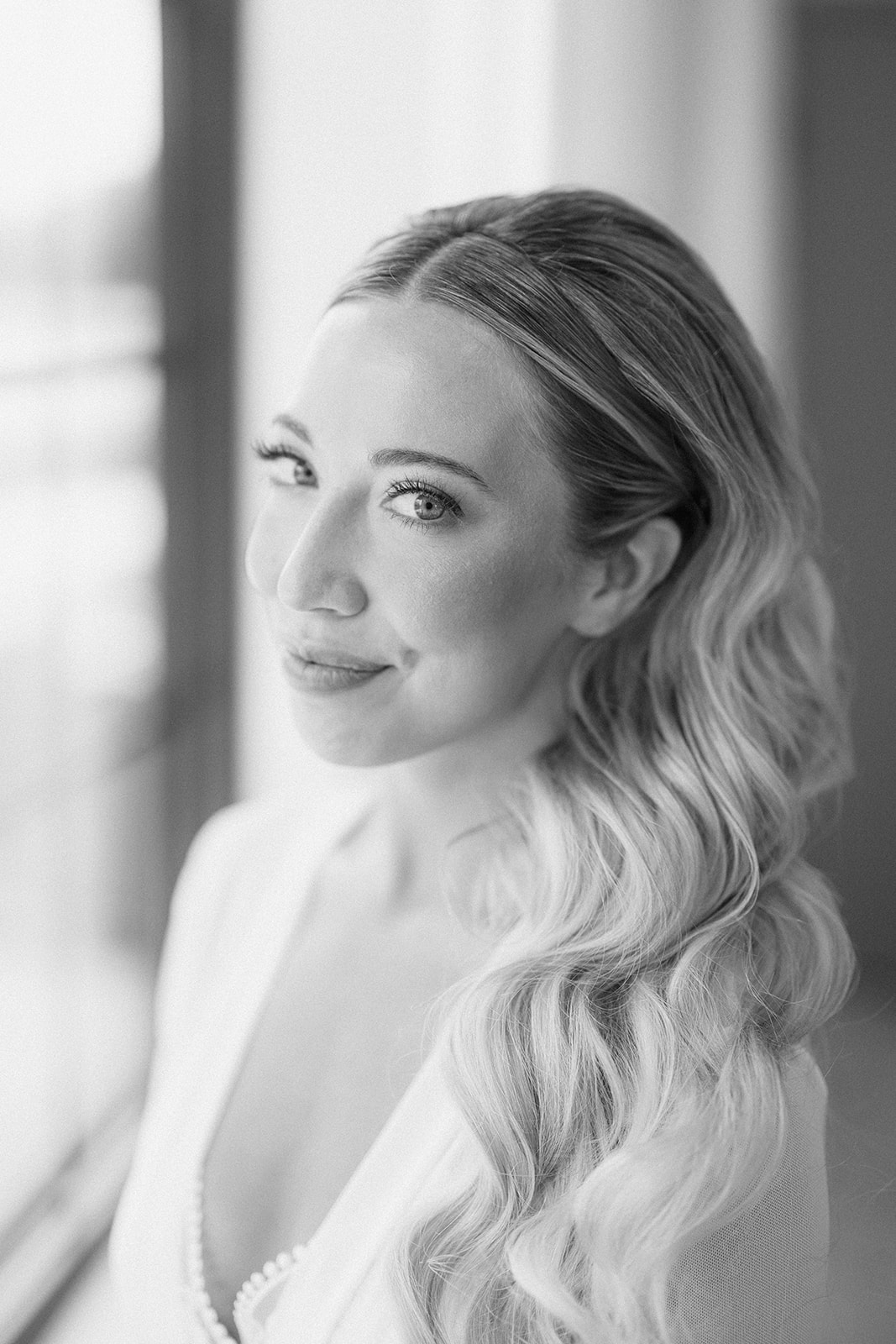 Black and white portrait of the bride in soft window light, her hair falling in long waves