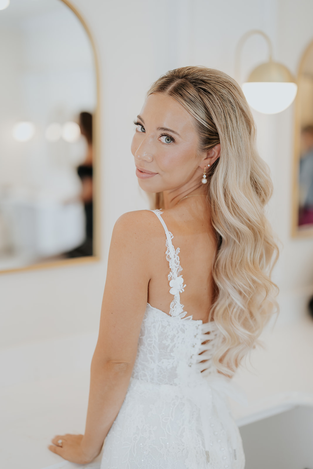 The bride glances over her shoulder in her lace gown, long blonde waves down her back