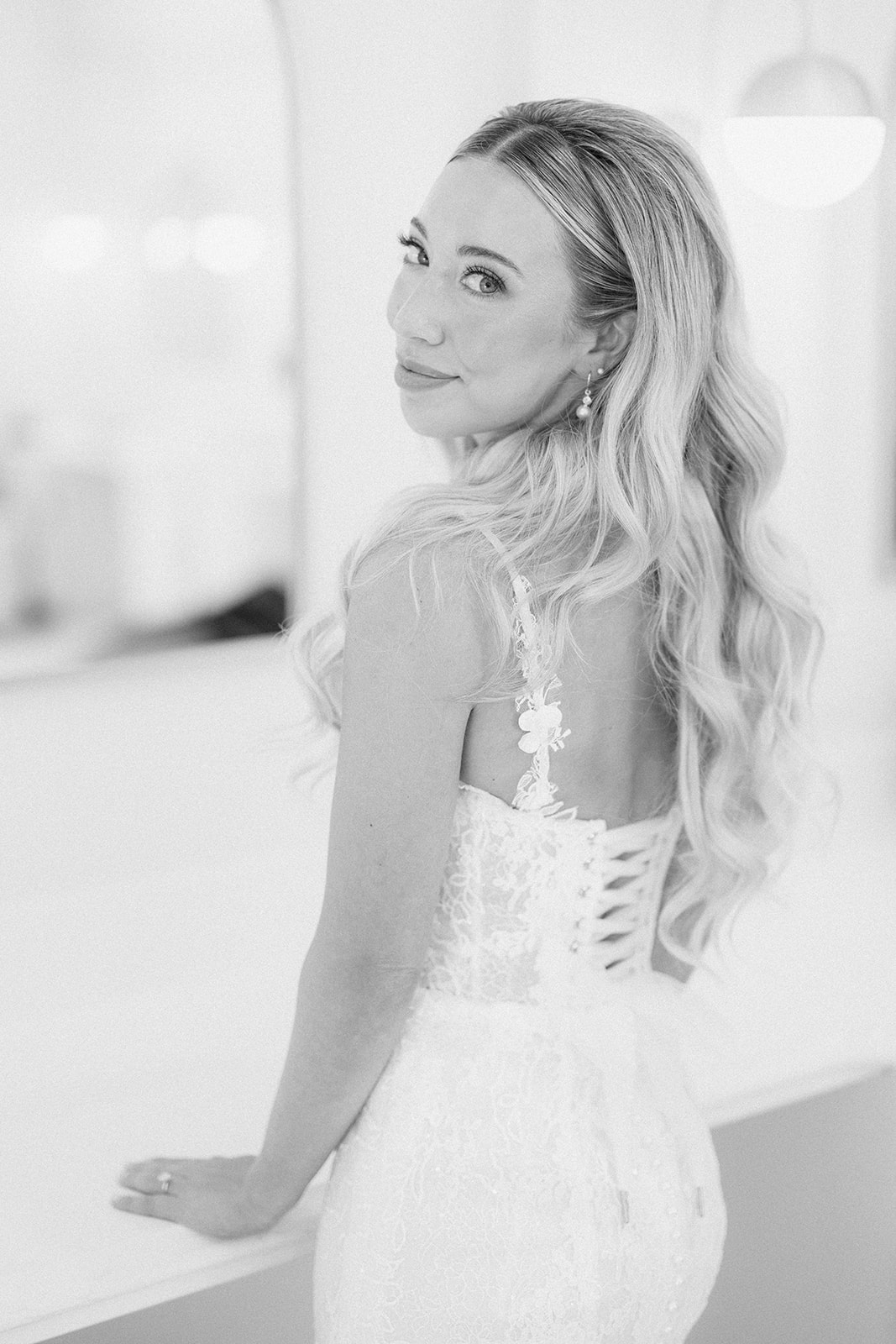 Black and white portrait of the bride looking over her shoulder, showing the lace-up back of her gown