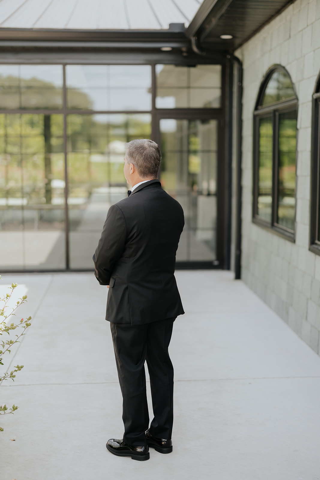 The bride's father waits with his back turned outside the venue, ready for their first look