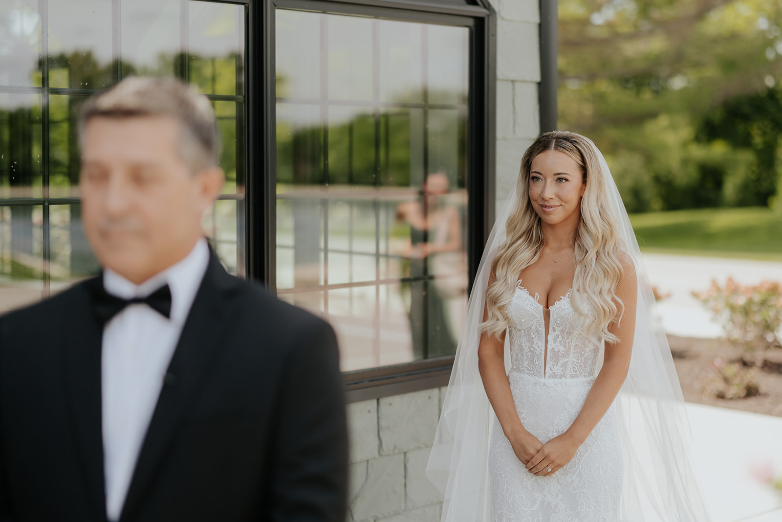 The bride walks up behind her father for their first look, smiling with her hands clasped
