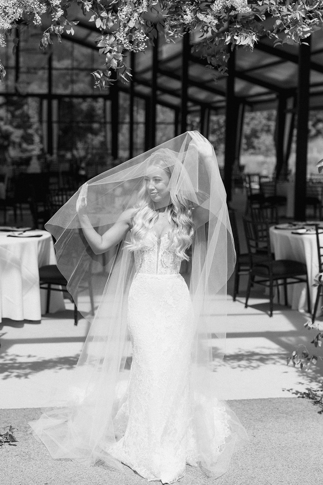 Black and white photo of the bride lifting her cathedral veil in an open-air pavilion