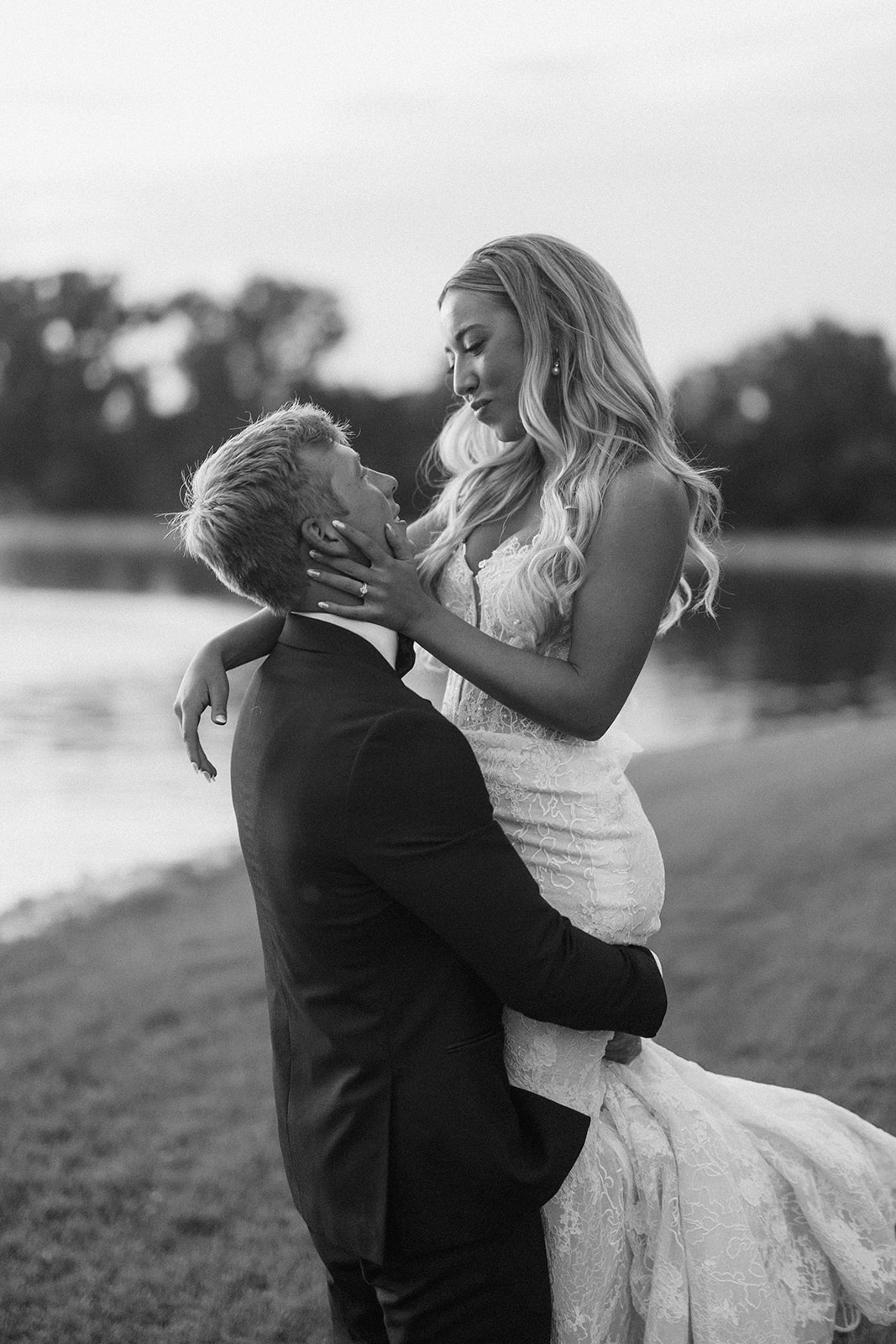 Black and white photo of Grant lifting Lauren beside the water at sunset