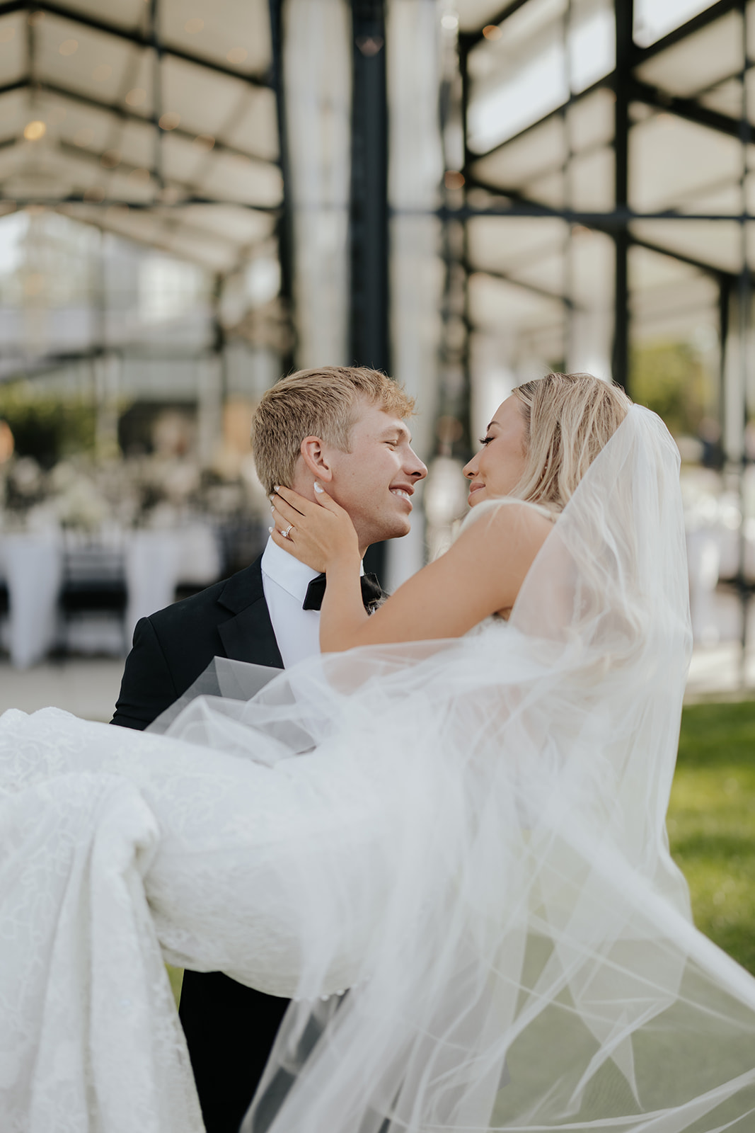 Grant carries Lauren in his arms as they laugh together, her veil flowing