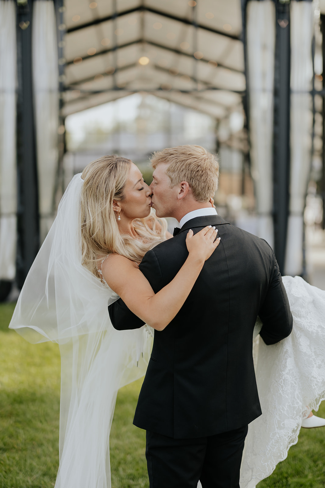Grant holds Lauren up for a kiss on the lawn, her gown and veil trailing