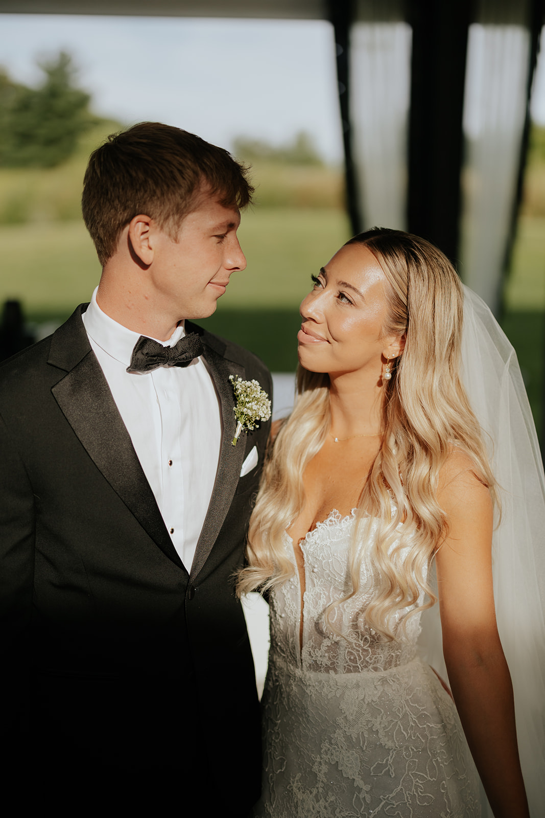 The bride gazes up at the groom in warm golden light beside the pavilion curtains