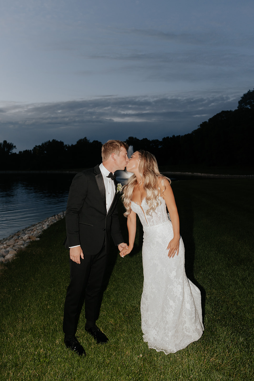 Lauren and Grant share a kiss at blue hour beside the pond and fountain