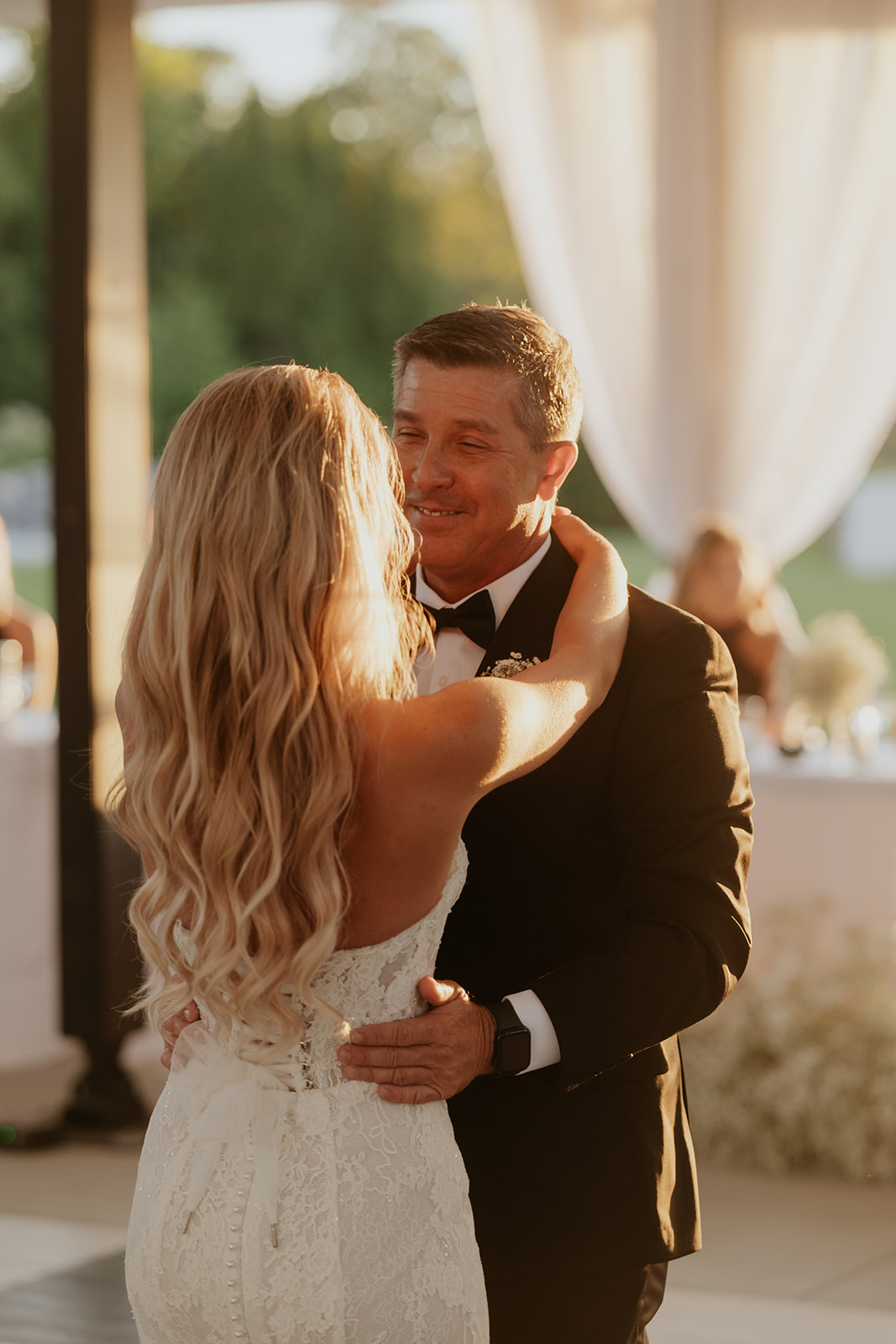 The bride and her father share a smiling father daughter dance in the warm evening sun